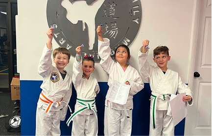 Kids in white gis holding up their class awards